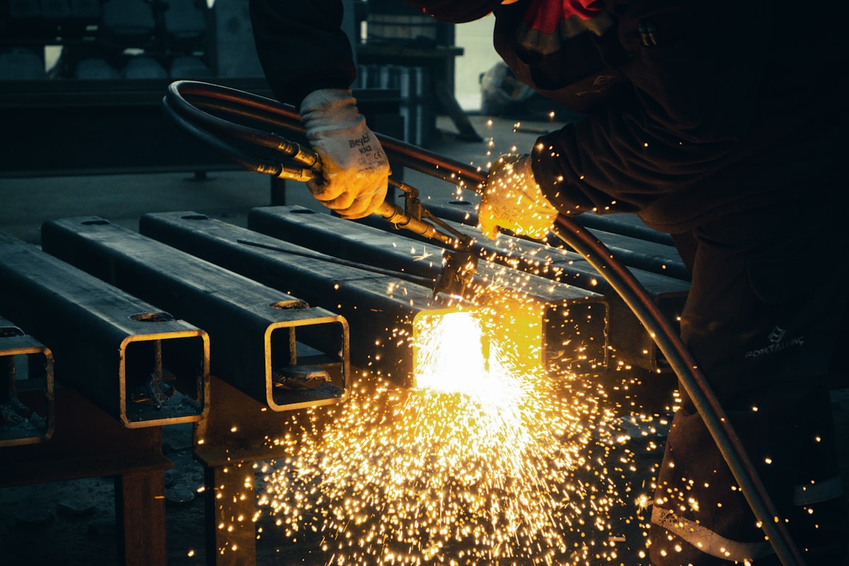 Factory worker welding metal with bright sparks for Litemask™ UV maskant surface protection during grit blast and shot